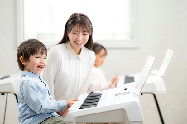 Pelajaran musik, dengan siswa yang sedang memainkan keyboard sedangkan guru mengawasinya sambil duduk di sampingnya