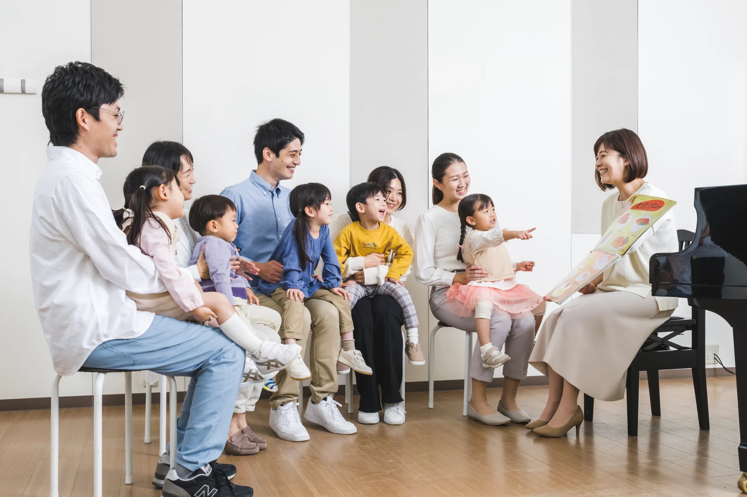Music teacher engaging a group of young children and parents during an early childhood music class at a Yamaha Music School, with a colorful
                                book and a grand piano in the scene.