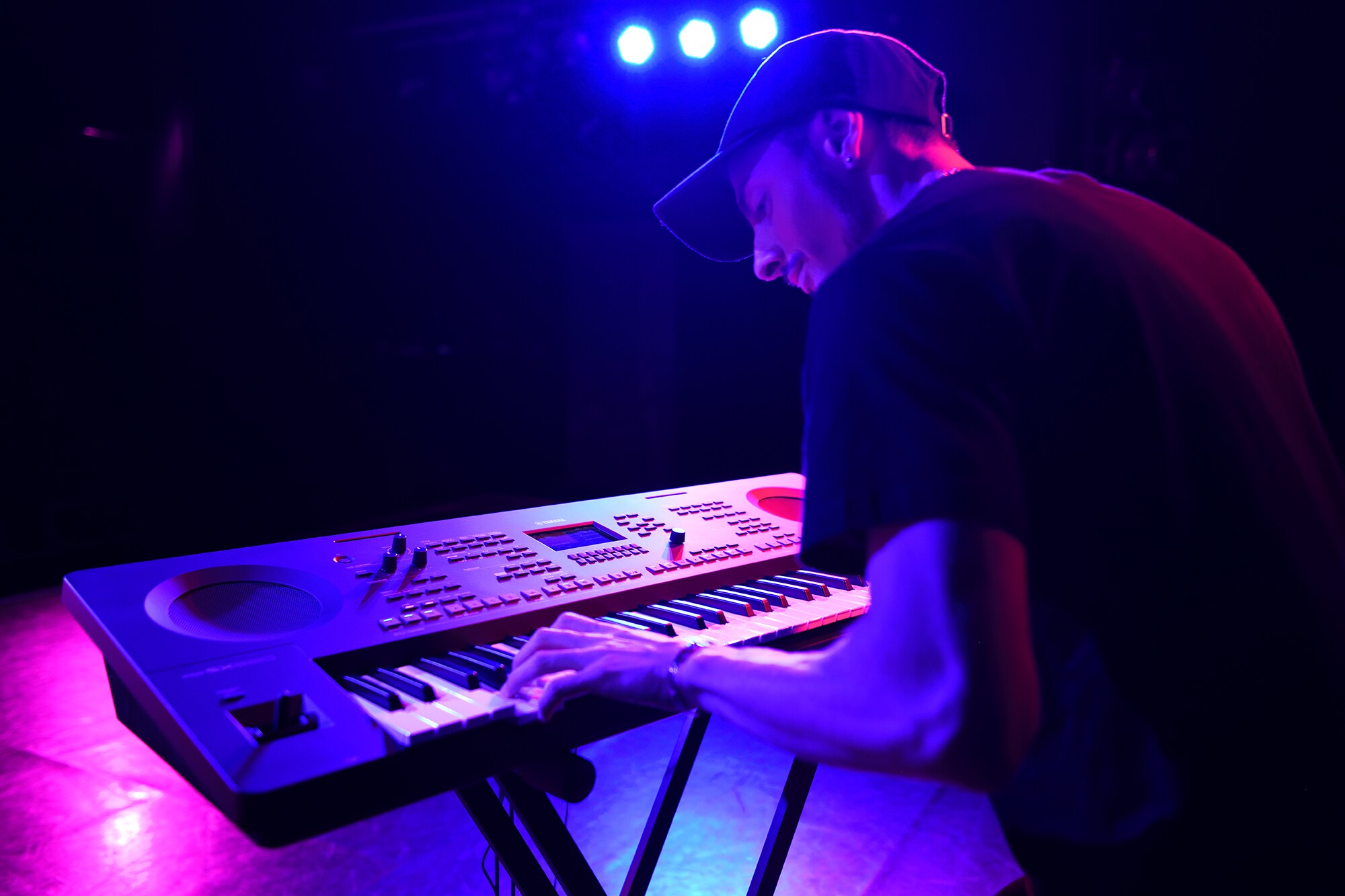 Seseorang yang memainkan arranger workstation Yamaha dengan stand di bawah pencahayaan panggung