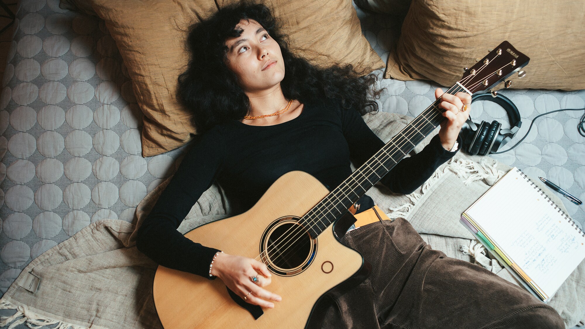 Person lying on a bed playing the TAG3 C acoustic guitar.