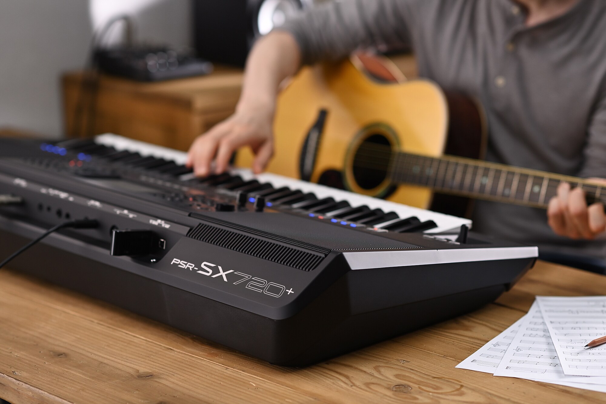 Foto seseorang yang memainkan Yamaha Arranger Workstation PSR-SX720+ sambil memegang gitar
