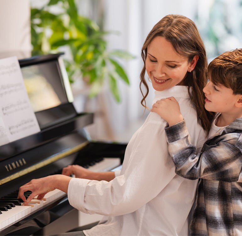 Seorang ibu dan anak perempuannya sedang asyik bermain piano upright B series