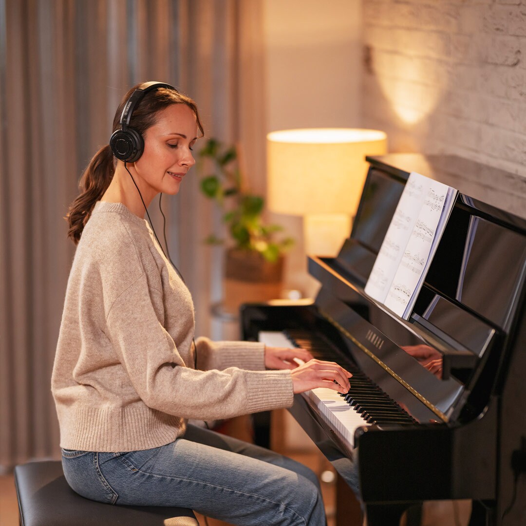 Seorang wanita sedang asyik bermain piano sambil mengenakan headphone