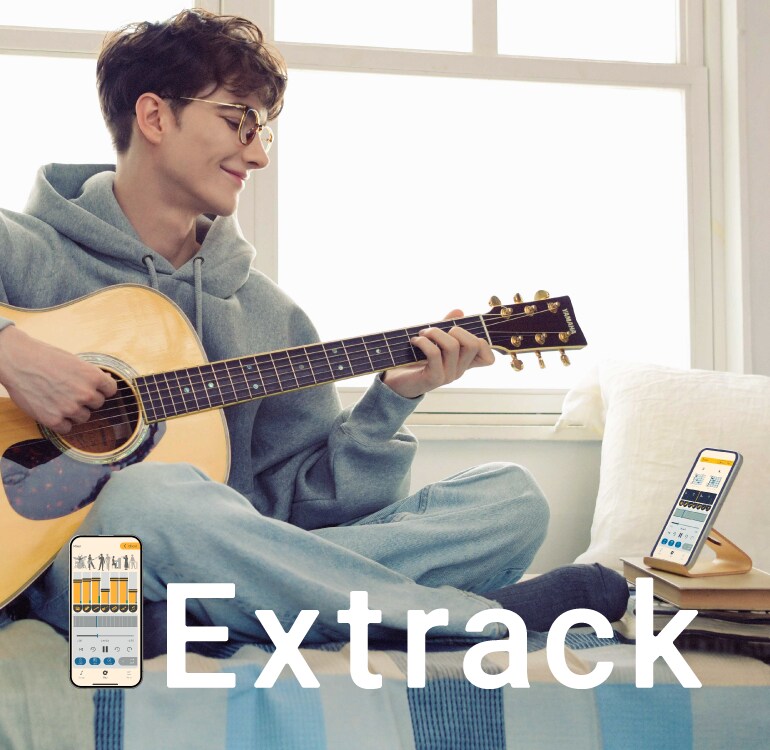 Seorang pria menikmati berlatih gitar sambil duduk di sofa dan bermain bersama dengan aplikasi latihan musik Extrack