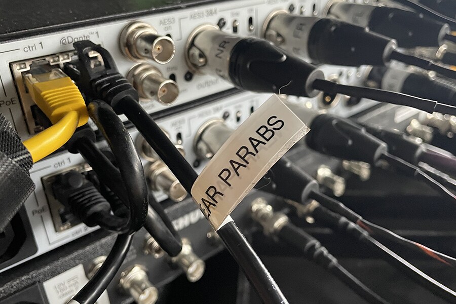  Close-up koneksi  perangkat audio yang  menampilkan kabel jaringan Dante dan output mikrofon parabola.