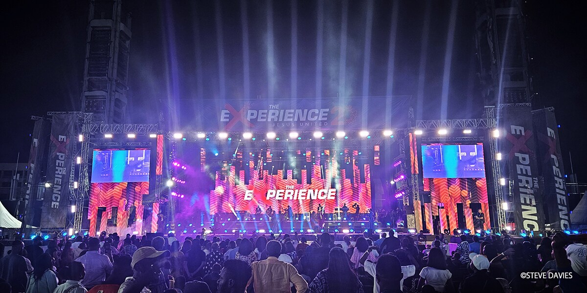 Tampilan  luas The Experience 2025 di Lagos, Nigeria, yang menampilkan  panggung  outdoor besar dengan pencahayaan dan layar video, di hadapan  ribuan jemaat  dalam acara musik gospel tahunan tersebut.
